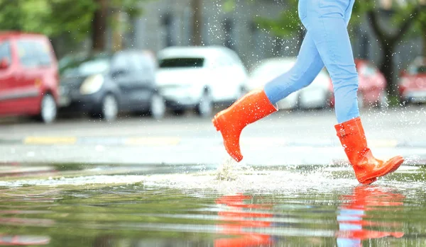 Woman with red rubber boots running in puddle, closeup. Rainy weather