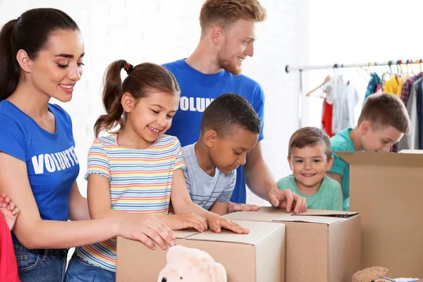 Voluntarios con niños clasificando bienes de donación en interiores — Foto de Stock