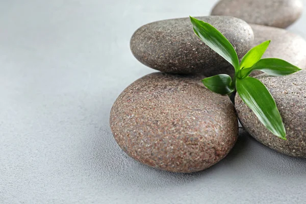 Pile of spa stones and green leaves on grey table, space for text — Stock Photo, Image