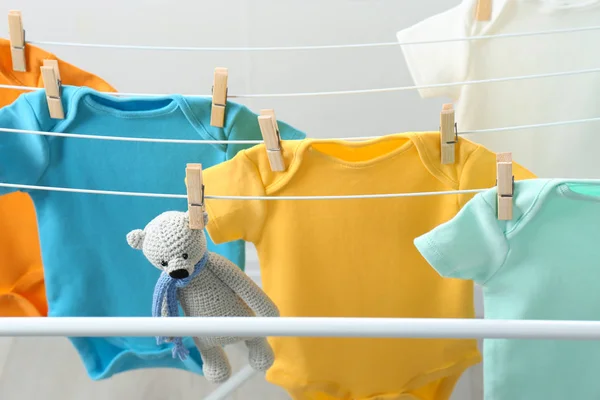 Diferentes onesies bebê bonito e urso de brinquedo pendurado na linha de roupas. Dia de lavandaria — Fotografia de Stock