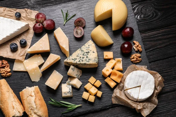 Composição de leigos planos com diferentes tipos de deliciosos queijos no tabuleiro de ardósia — Fotografia de Stock