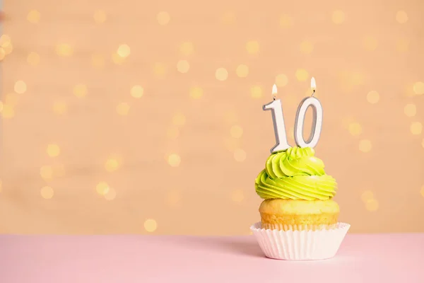 Cupcake d'anniversaire avec numéro dix bougie sur la table contre les lumières festives, espace pour le texte — Photo