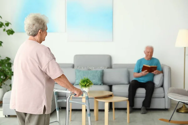 Elderly woman using walking frame and her husband at home