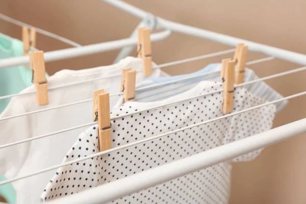 Different cute baby onesies hanging on clothes line against beige background, closeup. Laundry day — Stock Photo, Image