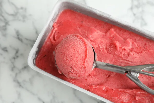 Container with delicious pink ice cream and scoop on marble table, top view — Stock Photo, Image