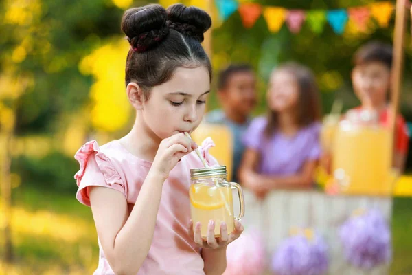 Cute little girl drinking natural lemonade in park, space for text. Summer refreshing beverage — Stock Photo, Image