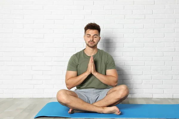 Hombre joven practicando yoga zen cerca de la pared de ladrillo blanco — Foto de Stock