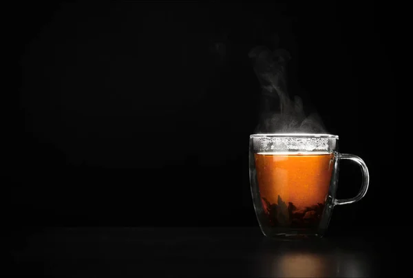 Стеклянная чашка горячего листового чая на столе на черном фоне, место для текста — стоковое фото