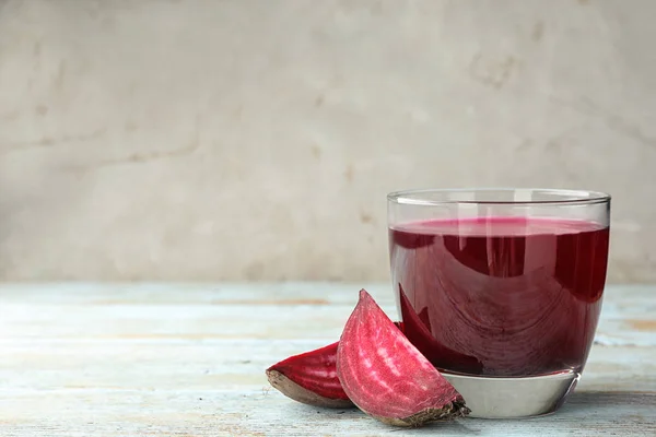 Cut beet and glass of juice on wooden table against grey background. Space for text — Stock Photo, Image