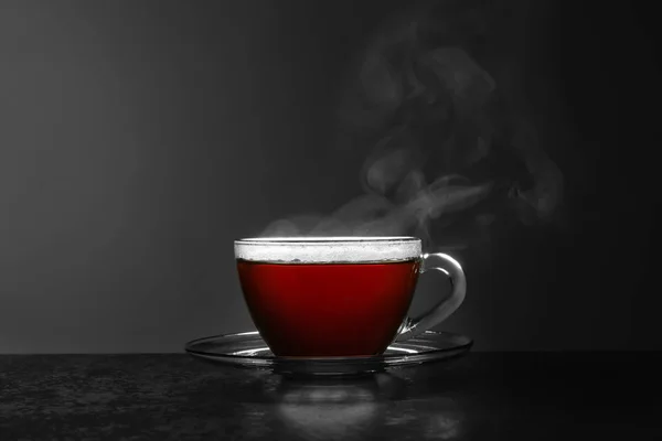 Skleněný pohár horkého čaje na kamennou stole proti šedém pozadí, prostor pro text — Stock fotografie