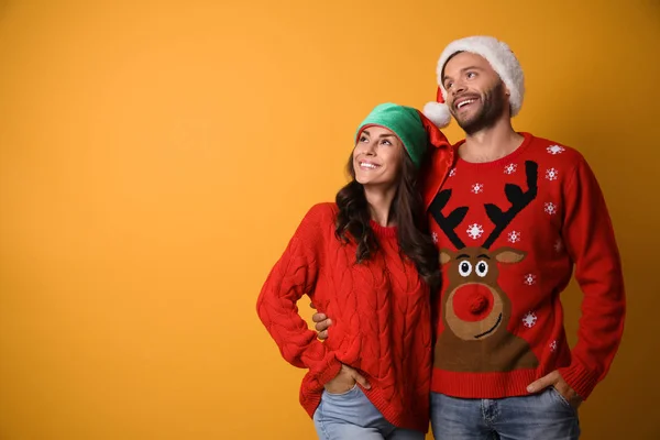 Young couple in Christmas sweaters and hats on yellow background. Space for text — Stock Photo, Image