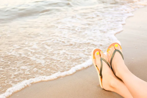 Primer plano de la mujer con chanclas con estilo en la arena cerca del mar, espacio para el texto. Accesorios de playa — Foto de Stock