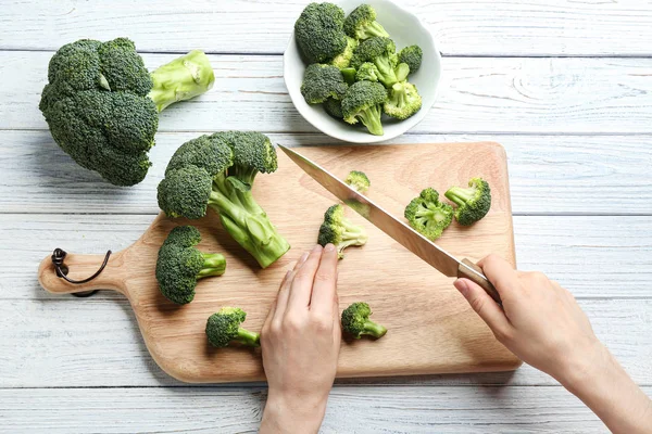 Wanita memotong brokoli hijau segar dengan pisau di meja kayu putih, pemandangan atas — Stok Foto