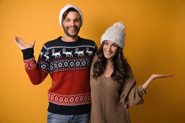 Fiatal pár karácsonyi pulóverek és kalapok a sárga háttér — Stock Fotó