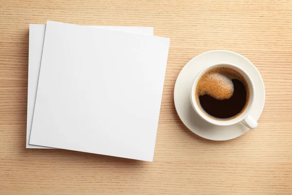 Blanco papieren vellen voor brochure en kopje koffie op houten achtergrond, platte lag. Mock up — Stockfoto