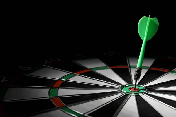 Green arrow hitting target on dart board against black background. Space for text — Stock Photo, Image