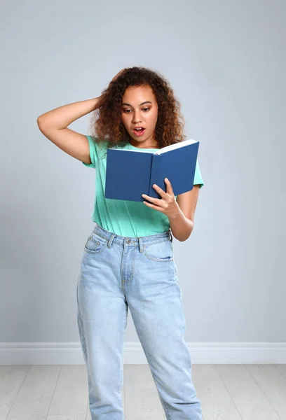 Mulher afro-americana bonita ler livro perto de parede clara dentro de casa — Fotografia de Stock