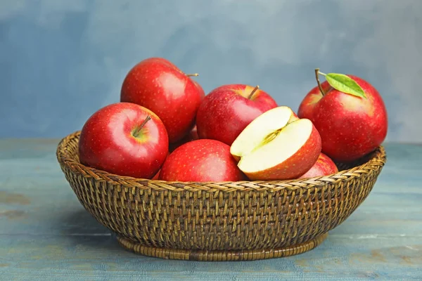 Bol en osier avec des pommes rouges juteuses mûres sur une table en bois sur fond bleu — Photo