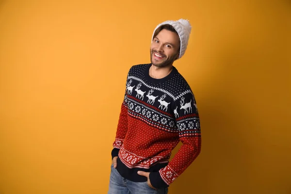 Young man in Christmas sweater and hat on yellow background