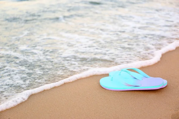 Des tongs élégantes sur le sable près de la mer, espace pour le texte. Accessoires de plage — Photo