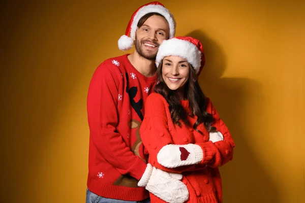 Jovem casal em camisolas de Natal e chapéus no fundo amarelo — Fotografia de Stock
