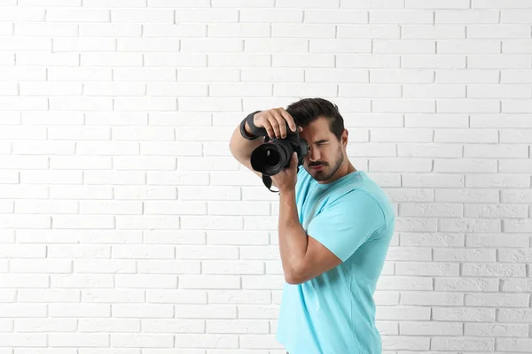 Young professional photographer taking picture near brick wall. Space for text — Stock Photo, Image