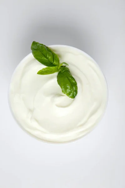 Bowl of fresh sour cream with basil on white background, top view — Stock Photo, Image