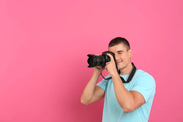 Young professional photographer taking picture on pink background. Space for text — Stock Photo, Image
