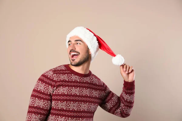 Happy young man in Christmas sweater and Santa hat on beige background — Stock Photo, Image