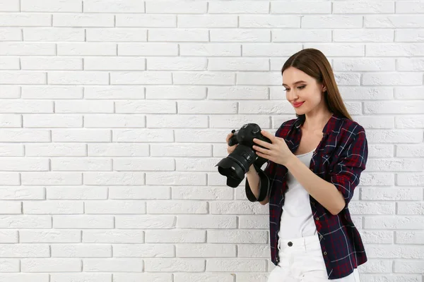 Fotógrafo profissional com câmera moderna perto da parede de tijolo branco. Espaço para texto — Fotografia de Stock