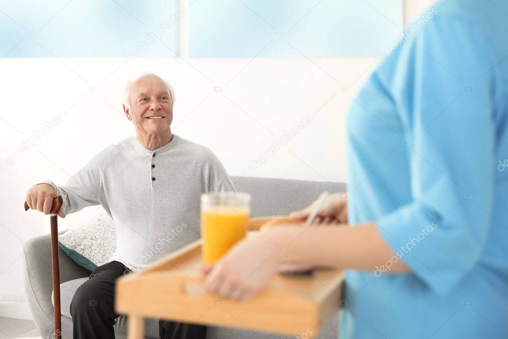 Nurse serving breakfast to elderly man indoors. Assisting senior people