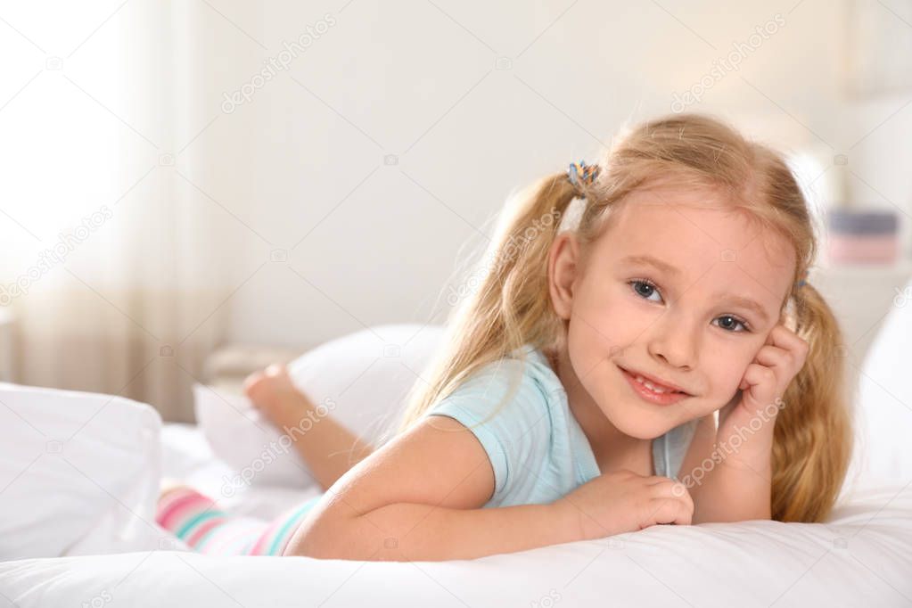 Portrait of cute little girl resting on large bed