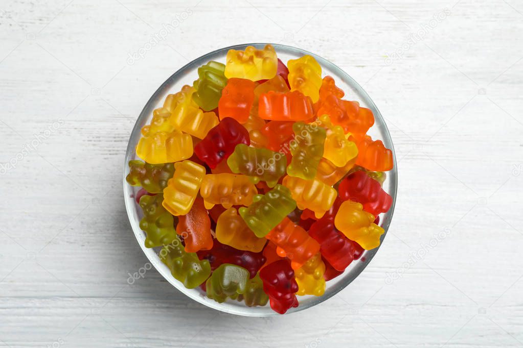 Bowl with delicious bright jelly bears on white wooden table, top view