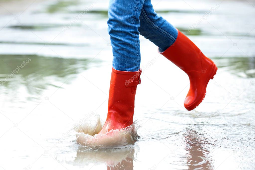 Woman with red rubber boots running in puddle, closeup. Rainy weather