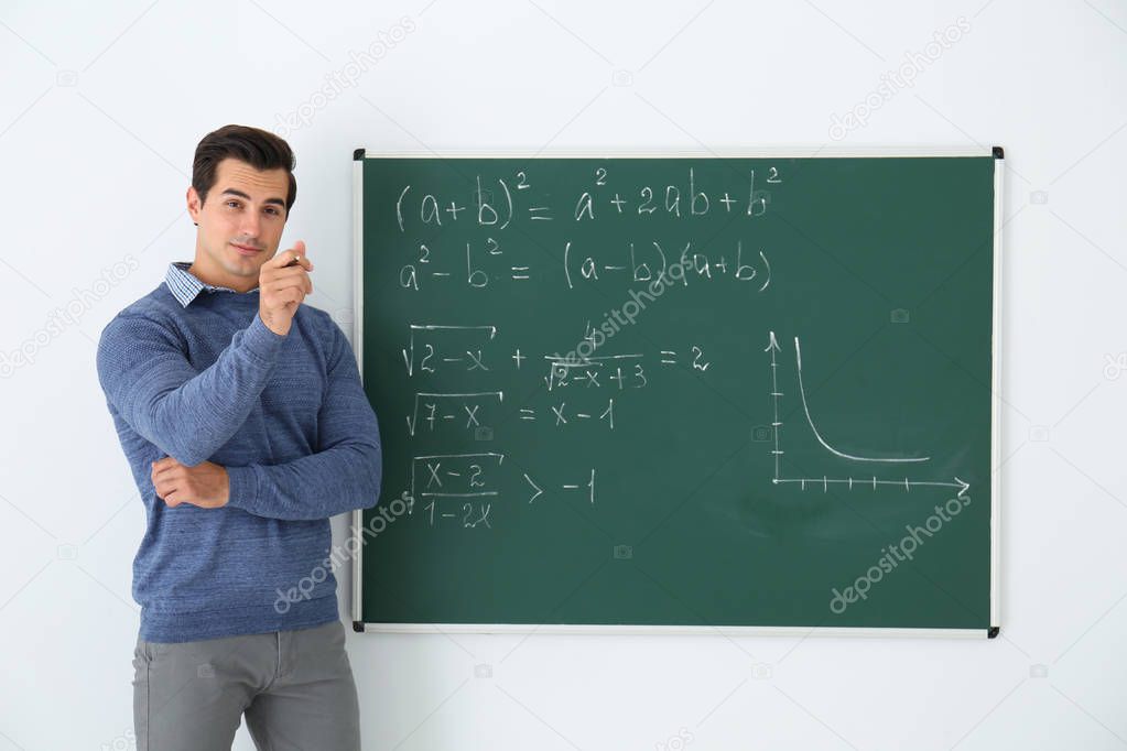 Young teacher near chalkboard with math formulas in classroom