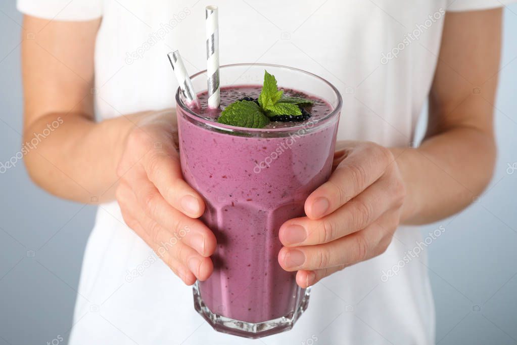 Young woman holding glass of tasty blackberry smoothie, closeup
