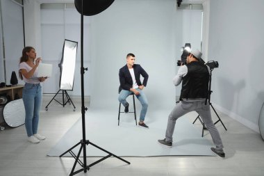Asistan modern stüdyoda genç adamın fotoğrafını çeken profesyonel fotoğrafçı