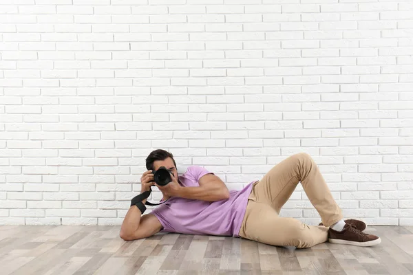 Ung professionell fotograf tar bild nära tegelvägg. Utrymme för text — Stockfoto