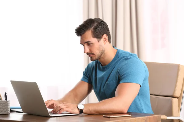 Handsome young man working with laptop at table in office — Stock Photo, Image