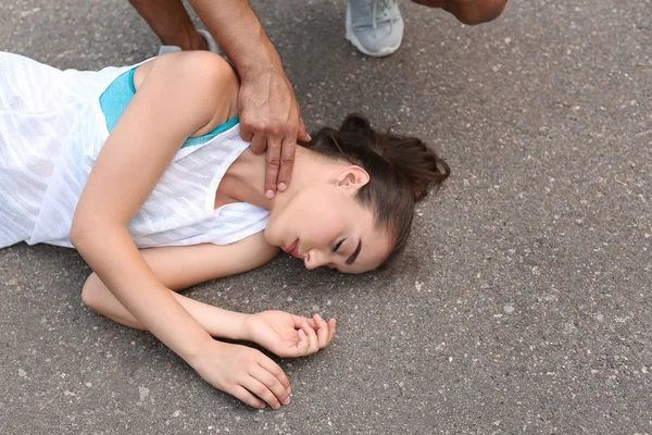 Young man checking pulse of unconscious woman on street — Stock Photo, Image