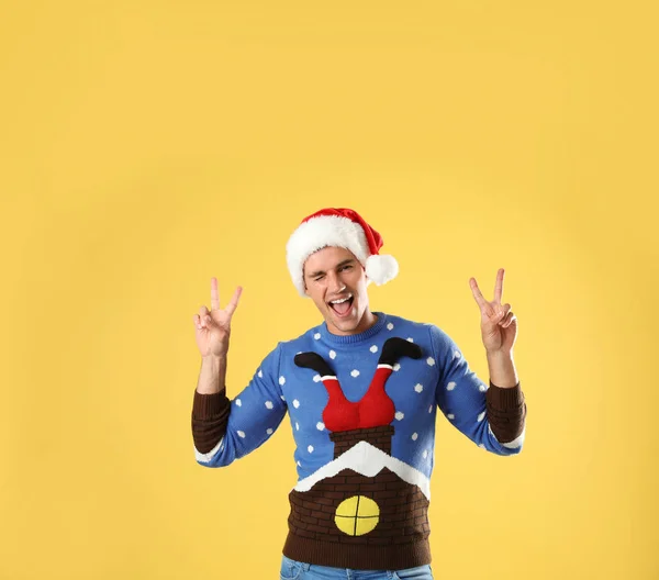 Portrait of young man in Christmas sweater and Santa hat on yellow background — Stock Photo, Image