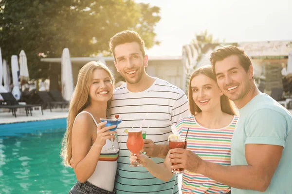 Mutlu genç arkadaşlar taze yaz kokteylleriyle yüzme havuzunun yanında dinleniyorlar.