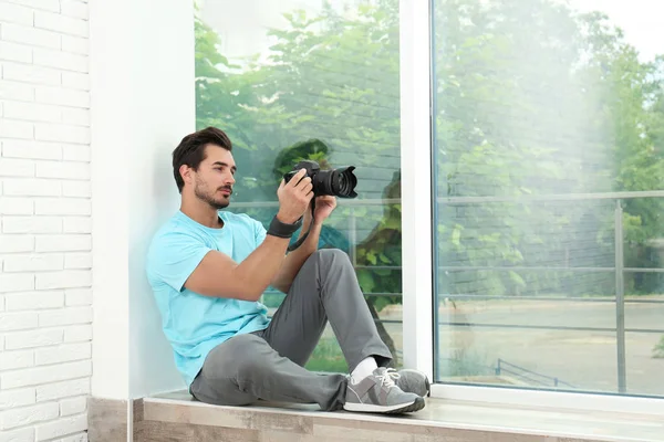Ung fotograf med professionell kamera nära fönster inomhus. Utrymme för text — Stockfoto