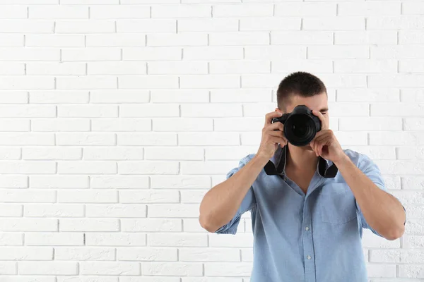 Jovem fotógrafo profissional tirando fotos perto da parede de tijolo. Espaço para texto — Fotografia de Stock