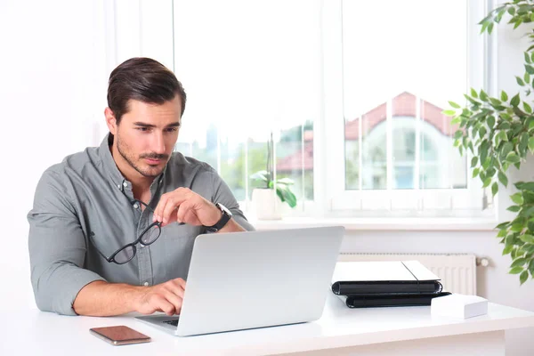 Jovem bonito trabalhando com laptop à mesa no escritório — Fotografia de Stock