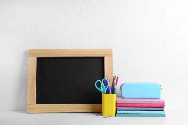 Chalkboard pequeno em branco e artigos de papelaria de escola diferentes na mesa de madeira perto da parede branca. Espaço para texto — Fotografia de Stock