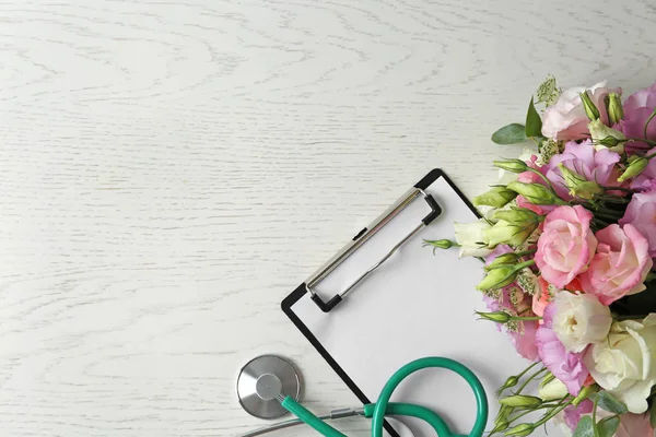 Επίπεδη σύνθεση με στηθοσκόπιο και λουλούδια σε λευκό ξύλινο φόντο, χώρο για το κείμενο. Παγκόσμια ημέρα υγείας — Φωτογραφία Αρχείου