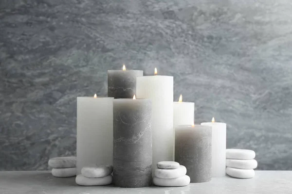 Conjunto de velas acesas com pedras de spa na mesa contra fundo de mármore cinza — Fotografia de Stock