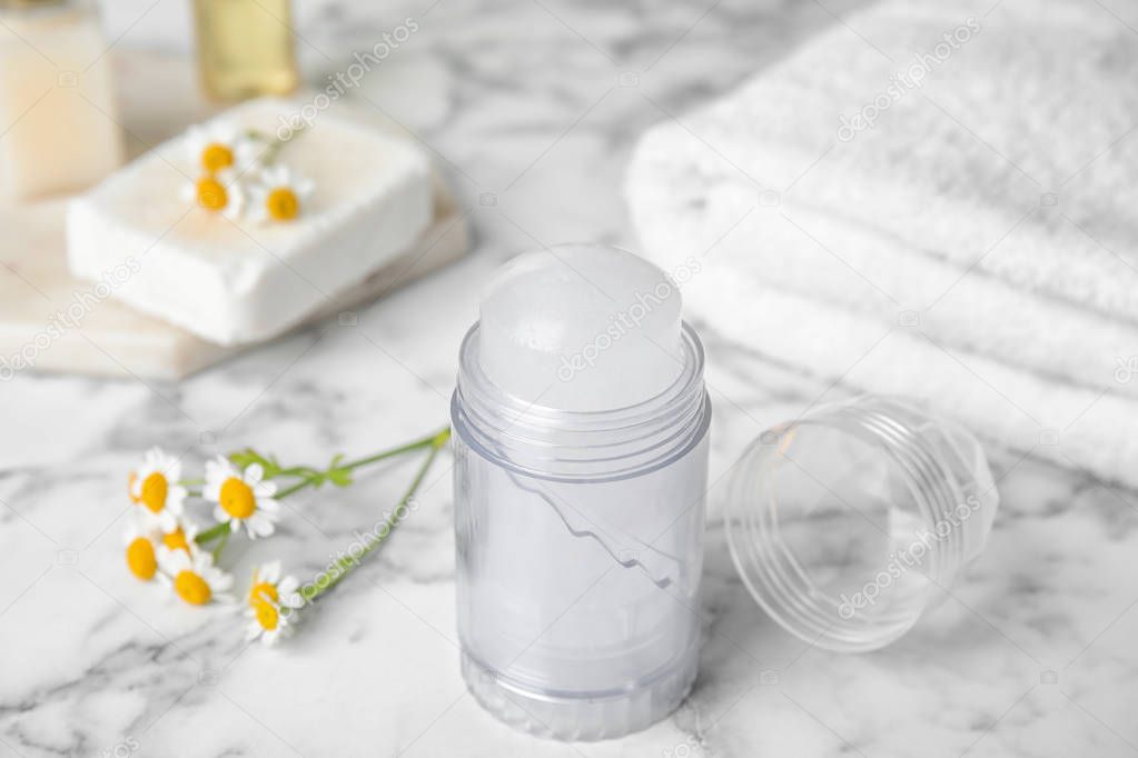 Natural crystal alum deodorant and chamomile flowers on white marble background