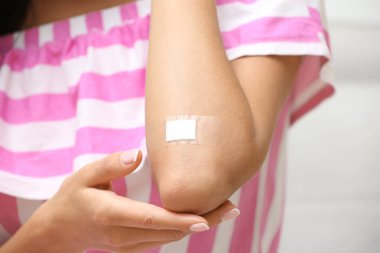 Hafif arka plana karşı dirsek üzerinde yapışkan bandaj ile kadın, closeup